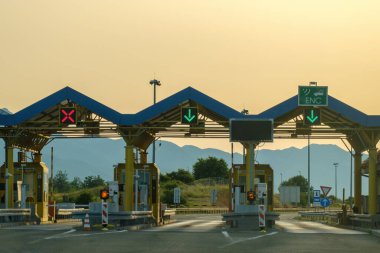 Paid expressway checkpoint tollgate shows right direction on highway. Expressway green signs allow driving against hills at back sunset