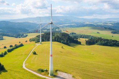 Aerial view of wind turbines propeller in the yellow field with amazing view on the mountains in sunny day. Environment friendly and renewable energy resource. 