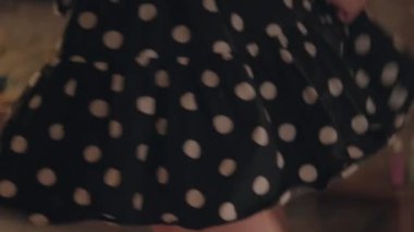 Woman dances in room holding black polka-dot dress hem on blurry background. Lady enjoys nice vacation dancing and turning around closeup