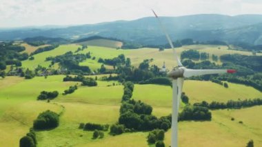 Aerial view of wind turbines propeller in the yellow field with amazing view on the mountains in sunny day. Environment friendly and renewable energy resource. 