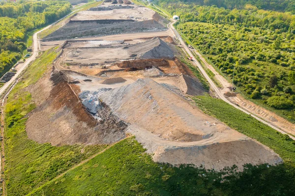Quarry for mining of natural resources on the hill close to the forest, aerial view