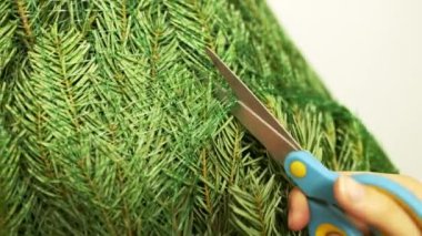 Noel ağacı hediye paketini açmak için mavi makas kullanıyor. Sahibi, oyuncaklarla Noel ağacı süslemeye hazırlanırken ambalajı kesti