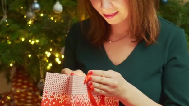 姜汁女士坐在圣诞树旁 用装饰红包打开礼物 脸上带着惊讶和微笑的表情 红头发的女士喜欢庆祝 — 图库视频影像