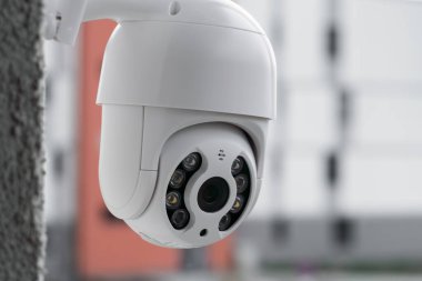 Arka planında çok katlı bulanık bir bina olan duvardaki modern CCTV kamerası. Hırsızlara karşı korumak için dışarıyı gözetliyor ve izliyoruz. 