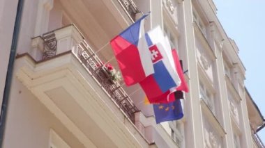 Güneşli bir günde balkonda sallanan hafif rüzgarda farklı Avrupa ülkelerinin bayrakları sallanıyor. AB bayraklı beyaz bina güneş ışığıyla aydınlanıyor