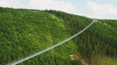 Turistler Dolni Morava 'daki derin vadi üzerinde uzun süspansiyonlu Gökyüzü Köprüsü üzerinde yürüyorlar. Dağlar ağaçlar ve çimlerle kaplı güneşli mavi gökyüzü manzarasının altında