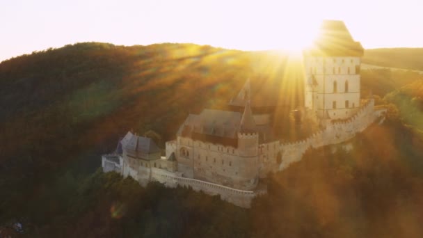 古代ゴシック様式のカルルシュタイン城は 明るい日差しの中で緑に囲まれています 日没の空中ビューで高地に建てられた国立遺産 — ストック動画