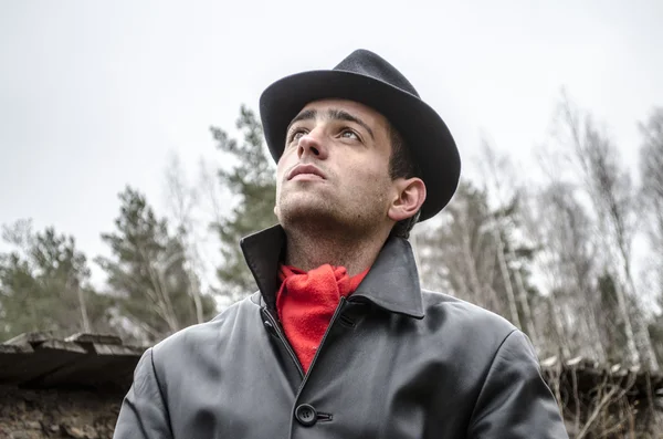 Een jonge man in een zwarte mantel en een hoed — Stockfoto