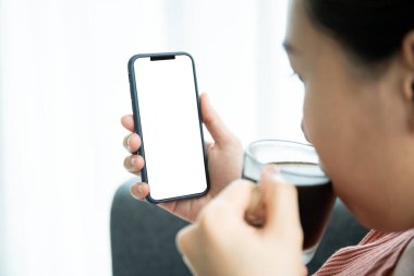 İzole edilmiş boş ekranlı akıllı telefonu taklit et. Genç Asyalı bir kadın sabah kahve içerken akıllı telefonuyla sosyal medyayı araştırıyor. Genç bayan sabahları bir fincan kahve içiyor..