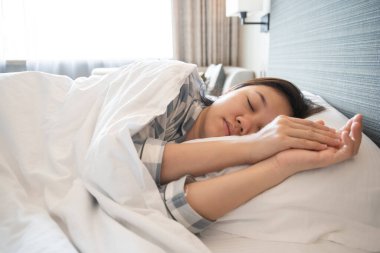 Güzel Asyalı genç kadın yatakta uyuyor ve gülümsüyor, kadın sabahın geç saatlerinde uyanıyor..