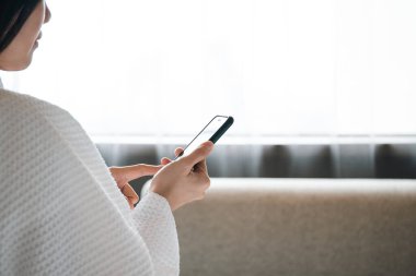 Sosyal medya ya da sosyal medya için yatak odasında akıllı telefon kullanan bornoz ya da duş takımı giymiş tanınmayan Asyalı genç bir kadın..