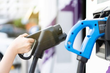 DC 'yi tutan tanınmayan Asyalı kadın - EV şarj istasyonunda CCS tip 2 EV konnektörü, bir EV-elektrikli araç hazırlayan kadın bir aracı şarj etmek için konnektör.
