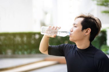 Aktif Asyalı sporcu açık hava koşusu ve antrenmandan sonra şişede su içiyor. Asyalı adam egzersize ara verdiğinde su içer. Sağlıklı bir adam kardiyo çalışması için çok çalışıyor..