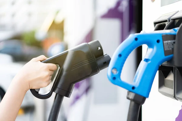 DC 'yi tutan tanınmayan Asyalı kadın - EV şarj istasyonunda CCS tip 2 EV konnektörü, bir EV-elektrikli araç hazırlayan kadın bir aracı şarj etmek için konnektör.