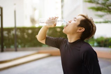 Aktif Asyalı sporcu açık hava koşusu ve antrenmandan sonra şişede su içiyor. Asyalı adam egzersize ara verdiğinde su içer. Sağlıklı bir adam kardiyo çalışması için çok çalışıyor..