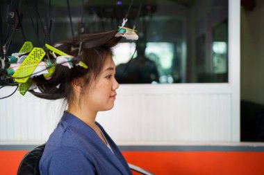 Güzel Asyalı genç bir kadın, profesyonel kuaförden saç maşası yapıyor. Modern dijital saç bigudisi kullanan bir kuaför..