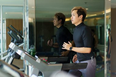 Aktif Asyalı sporcu koşu bandında spor ya da spor salonunda kardiyo çalışması yaparak kardiyo egzersizi yapıyor..