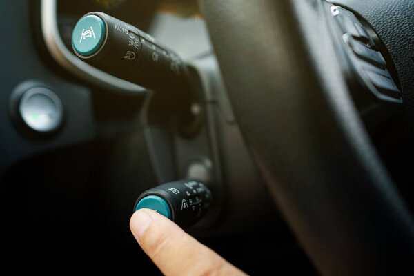 Unrecognizable man driver activating the adaptive cruise control or steering assistant on the control stick behind steering wheel  in electric vehicle - EV. Driving Assist system in modern car.