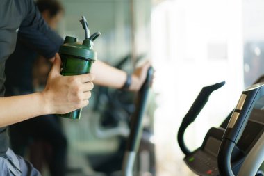 Aktif Asyalı genç adam eliptik egzersiz makinesinde kardiyo egzersizi yapıyor ve şişede su içiyor. Yağ yanığı ve kas yapısı. Vücut geliştirme konsepti.