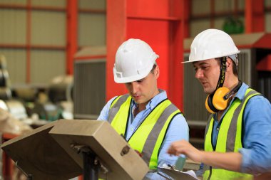 Kafkasyalı endüstriyel mühendis bir fabrikada çalışıyor ve birlikte tartışıyorlar. Metal işçiliği ölçen ve bir rapor belgesini inceleyen kıdemli mühendis veya müteahhit.