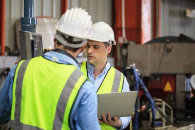 Kafkasyalı endüstriyel mühendis bir fabrikada çalışıyor ve birlikte tartışıyorlar. Metal işçiliği ölçen ve bir rapor belgesini inceleyen kıdemli mühendis veya müteahhit.