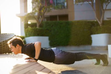 Aktif Asyalı genç adam vücut ağırlığı egzersizini yakın mesafeden yapıyor sporcu ise şınav ve kalasla vücut ağırlığı egzersizi yapıyor. Asyalı sporcu kas ve vücut geliştirme egzersizi yapıyor..