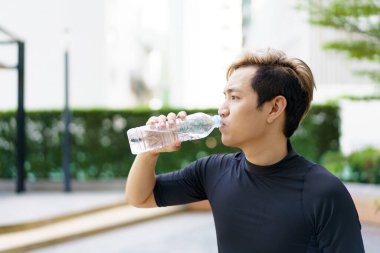 Aktif Asyalı sporcu açık hava koşusu ve antrenmandan sonra şişede su içiyor. Asyalı adam egzersize ara verdiğinde su içer. Sağlıklı bir adam kardiyo çalışması için çok çalışıyor..