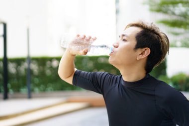 Aktif Asyalı sporcu açık hava koşusu ve antrenmandan sonra şişede su içiyor. Asyalı adam egzersize ara verdiğinde su içer. Sağlıklı bir adam kardiyo çalışması için çok çalışıyor..
