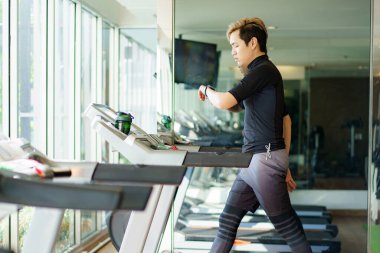 Aktif Asyalı sporcu koşu bandında spor ya da spor salonunda kardiyo çalışması yaparak kardiyo egzersizi yapıyor..