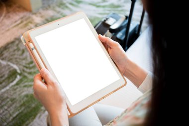 Model - boş ekran tableti kırpma ile izole edildi. Mutlu Asyalı genç kadın turist otelin yatak odasında yatakta oturuyor ve dijital tablet kullanıyor. İş kadını turist otelde dinleniyor.