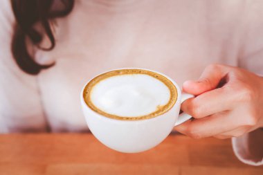 Tanımlanamayan Asyalı genç bir kadın elinde fotokopi alanı olan sıcak bir kahve fincanı tutuyor. Mutlu kız kahvecide latte içmekten hoşlanır. Sıcak içecek için modern seramik bardak.