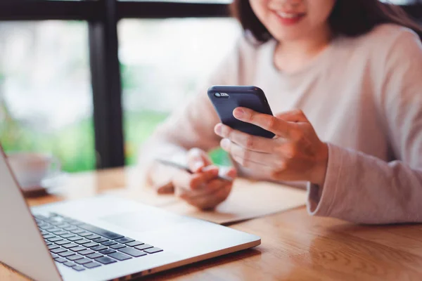 Tanımlanamayan neşeli genç iş kadını akıllı telefondan bir mesaj okuyor. Kafede kalırken dizüstü bilgisayar ve akıllı telefon üzerinde çalışan Asyalı bir kız. Çevrimiçi öğrenme kavramı.