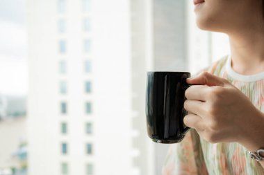Pencerenin yanında kahve fincanı tutan genç bir Asyalı kadın, kahve içen bir kadın. Sabahları sıcak kahve içen mutlu bir kadın fotokopi makinesiyle yakınlaşır..