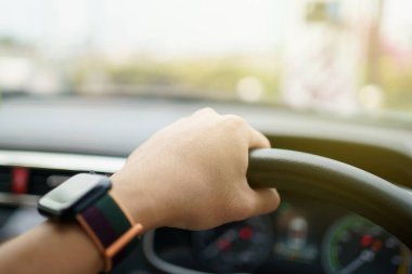 Tanımlanamayan bir erkek sürücü direksiyonda sol elini tutarak direksiyona geçiyor, adam araba kullanıyor. Adam araba kullanırken yolda güzel bir güneş ışığı. Güvenli sürüş kavramı.