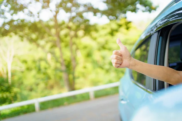 Unrecognizable Asian woman driver showing a thumb up outside the vehicle while driving a car. Happy woman driver or passenger showing her thumb up during in the car. Safety trip and freedom concept.