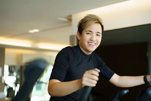 Active Asian young man making a cardio exercise on the elliptical exercise machine in the gym. Fat burn and body muscle building. bodybuilding workout concept.