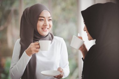 Cheerful Asian muslim businesswomen talking together in their workplace during the break. Two muslim woman in business casual dressed making a discussion together , diversity in nation and religion.