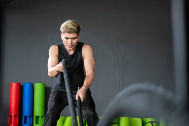 Güçlü Asyalı sporcu, kapalı bir salonda kopyalanmış halat egzersizi yapmak için hazır bekliyor. Güçlü genç sporcu vücut geliştirme konsepti geliştiriyor, kas geliştiriyor..