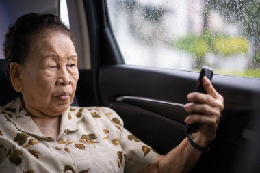 80-90 yaşları arasında çok yaşlı Asyalı bir yolcu kadın yağmur yağarken araba ile seyahat ediyor ve video kullanıyor. Fotokopi çekilen özel bir arabada neşeli bir emekli kadın..