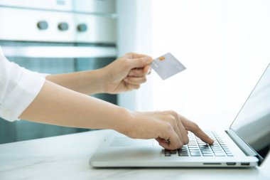 Unrecognizable cheerful Asian woman making an online payment via credit card for cooking online learning. The new normal online transaction in modern lifestyle concept with copyspace.