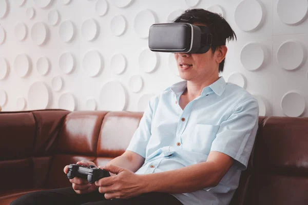 Asian retired old man relaxing in the living room and enjoy playing Virtual Reality (VR) video game. Leisure activity in elder people after their retirement. Asian old man and VDO game with copyspace.