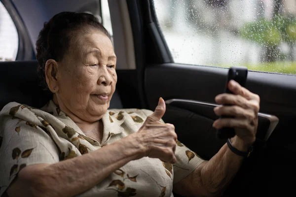 Very old Asian passenger woman age between 80 - 90 years old traveling by the car while raining and using a video call. Cheerful retired woman in a private car portrait with copy space.