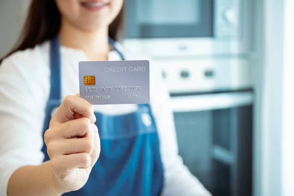 Unrecognizable cheerful Asian woman smiling and showing a credit card, a fake credit card, to the camera with copyspace. Financial and gastronomy, home interior concept. Happy woman show a credit card