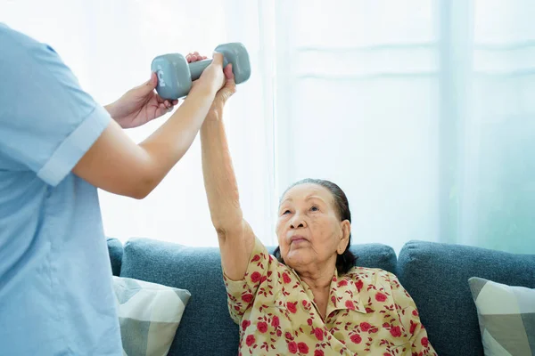 Asian elder woman doing a physical therapy exercise with her granddaughter by using dumbbells, wellness - wellbeing and health care in elder people in aging society concept.