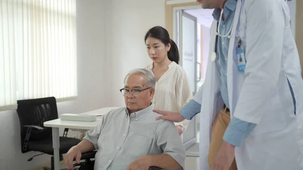 Granddaughter take her grandfather on wheelchair see the doctor or therapist at hospital. Health care and wellbeing in Asian family - aging society concept.