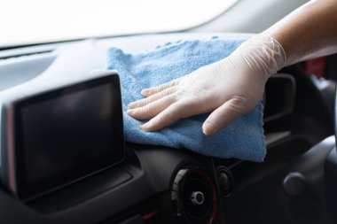 Cheerful Asian man cleaning and rubbing a car interior by using sponge and soft micro fabric. Professional worker polishing a car with car wax, auto care concept.