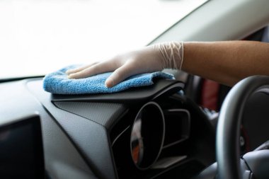 Cheerful Asian man cleaning and rubbing a car interior by using sponge and soft micro fabric. Professional worker polishing a car with car wax, auto care concept.