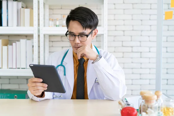 Professional Asian doctor working in the doctor office in hospital and looking at the tablet close up. Doctor working on the tablet with copyspace. Nutritionist specialist portrait close up.