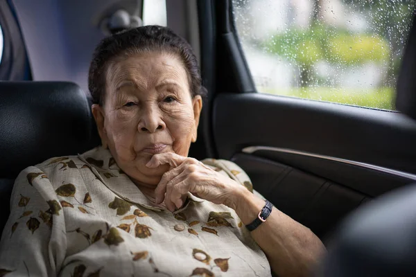 Very old Asian passenger woman age between 80 - 90 years old traveling by the car while raining. Cheerful retired woman in a private car portrait with copy space. Wellness and wellbeing in old people.