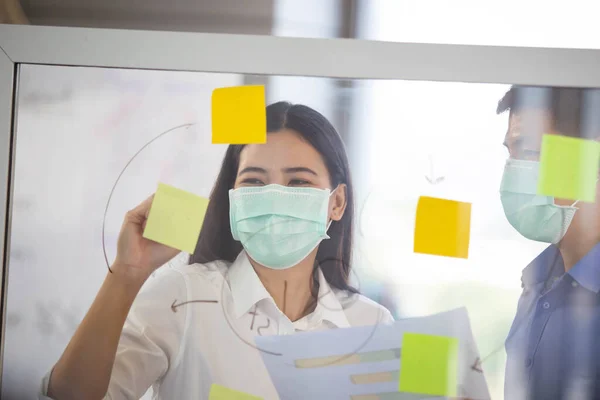 Group of senior businesspeople with hygiene protective face mask in meeting and discussing in the office, enterprise business meeting. Serious staff meeting in the workplace